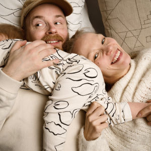 Muotoilijat Olli Sallinen ja Saana sipilä makoilevat nauravaisina sisustustyynyjen päällä. Vauva mönkii heidän päällään.
