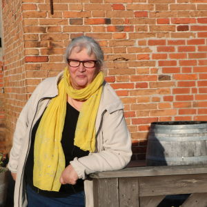 En kvinna i halsduk och glasögon framför en tegelvägg. 