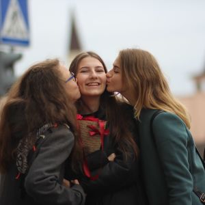 Kaksi tyttöä antaa suukon keskellään olevan kolmannen tytön poskelle.