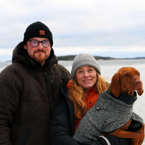 Simon Strömsund och Ida Törnroos står på en strand tillsammans med sin hund. 