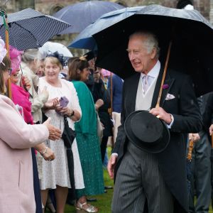 Kung Charles III ler brett med ett paraply i handen när han hälsar på gäster på ett trädgårdsparty i Edinburgh.