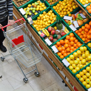 En person skuffar en kundvagn framför ett stort sortiment av bland annat citrusfrukter.
