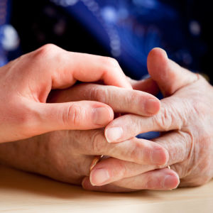 händer. en äldre persons knäppta händer och så en yngre människas hand ovanpå