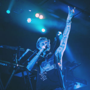 Rap-artisti Machine Gun Kelly seisoo lavalla mikki suunsa edessä ja käsi ilmassa sormet pirunsarvi-asennossa.