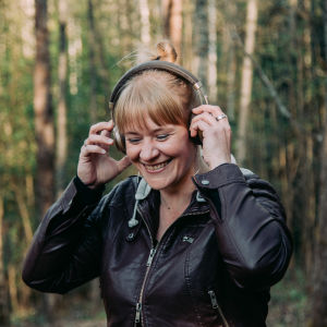 Nainen kuuntelee metsässä kuulokkeilla. 