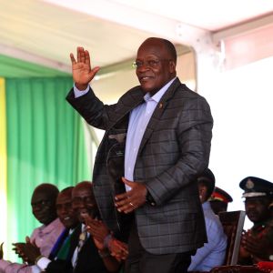 John Magufuli inledde en ny femårig presidentperiod i november. I juni deklarerade han att Tanzania är coronafritt. En äldre svart man i kostym står och vinkar med handen. Bakom honom sitter fler personer. John Magufuli inledde en ny presidentperiod i november 2020.