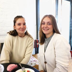 Sara Naydenov och Emma Backman sitter vid ett matbord och tittar leende in i kameran.