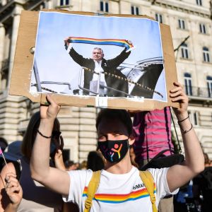 En demonstrant håller upp ett plakat med en bild på premiärminister Viktor Orbán. På bilden har någon redigerat in en regnbågsflagga som Orbán håller i.