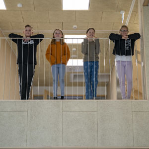 Fyra skolelever står på övre våningen i ett nybyggt skolhus och tittar ner.