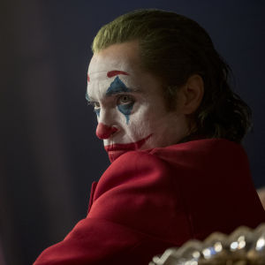 Närbild på Joker (Joaquin Phoenix) iklädd clownmask och röd kostym.