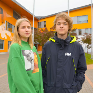 En flicka och en pojke framför en skolbyggnad.