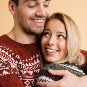 Man och kvinna i liknande stickade tröjor kramar om varandra och ler