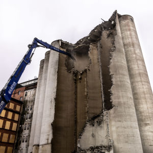 Rivningskran drar bort betong från silobyggnad