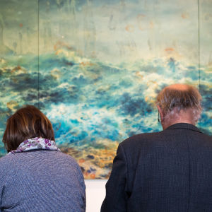 En kvinna och en man sitter på en bänk framför ett konstverk på ett museum. 