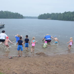 Ett tiotal barn och några vuxna kvinnor springer ut i vattnet vid en strand.