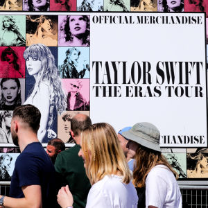Människor går framför en skylt där det står "Taylor Swift The Eras Tour Merchandise". På skylten finns massvis av bilder på Taylor Swift.