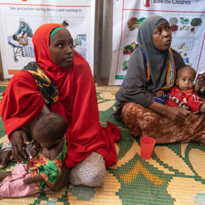 Kaksi somalialaista äitiä lapsineen istuu klinakan lattiamatolla, toisella punainen ja toisella vihreä kaapu. 