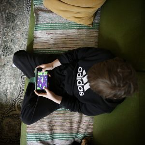 En pojke spelar ett mobilspel i en soffa.
