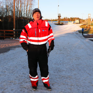 Juha Savolainen litar på att allt är i skick lagom till tävlingarna. Juha Savolainen iklädd orange overall framför en ett snöigt landskap i solsken.