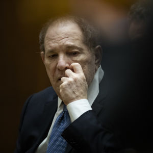 Harvey Weinstein kliar sig i ansiktet medan han tittar ner. Han sitter i en rättssal.