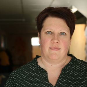 En kvinna med kort mörkt hår står i en mörk korridor.