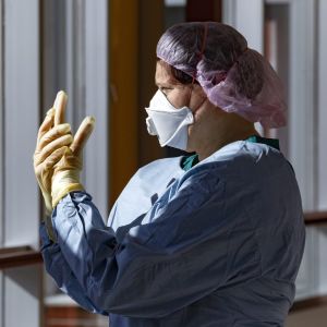 En sjukskötare i skyddsutrustning står vid ett fönster.