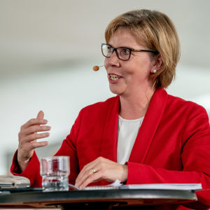 Anna-Maja Henriksson står vid ett bord och pratar under regeringens presskonferens i Helsingfors centrumbibliotek Ode den 3.6.2019.