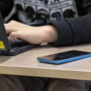 Oppilas työskentelee läppärillä, oppilaan kännykkä on vieressä pulpetilla.