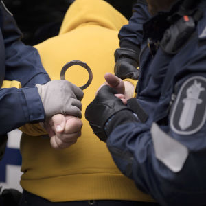 Poliisit laittavat käsirautoja pidätetyn käsiin.