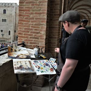 Akvarellpapper från Fabriano används av konstnärer över hela världen. Bilden är från Akvarellfestivalen i Fabriano 2018 En person står och målar i akvarell med utsikt över ett torg.