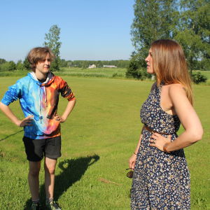 Två ungdomar samtalar med vuxen kvinnoantagen person i rural sommarmiljö.