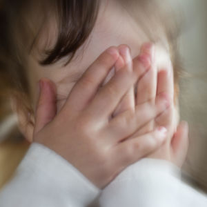 Litet barn täcker ansiktet med händerna. Illustrerande bild.