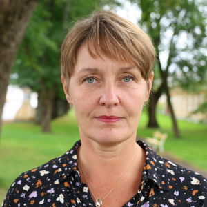 En kvinna med kort brunt hår står i en park.