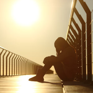 Person sitter ensam på brygga i solnedgången.