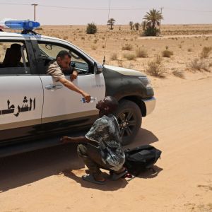 En libysk gränsvakt ger vatten till en migrant i Tunisien.