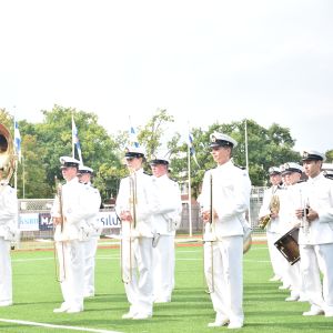 Militärorkester på sportplan med träd i bakgrunden.