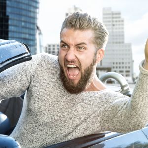Mies autossa nostaa käsivarttaan ylös huutaen.
