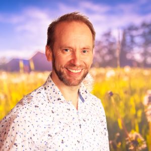 Erik-André Hvidsten ler rakt in i kameran, i bakgrunden syns en sommaräng.