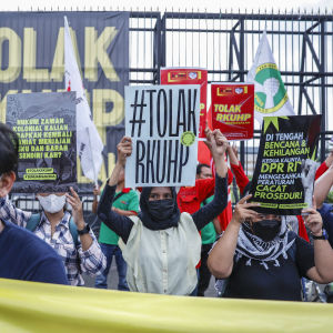 Kuvassa näkyy joukko mielenosoittajia kasvomaskit kasvoillaan. He pitävät käsissään kylttejä, joissa lukee uutta rikoslakia vastustavia tekstejä indonesian kielellä. 