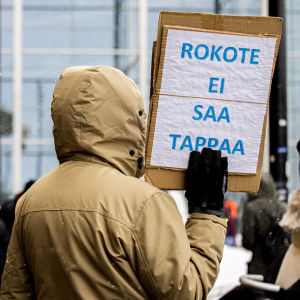 En demonstrant håller upp en skylt där det står "Ett vaccin får inte döda" under en coronademonstration i Helsingfors i mars 2021.