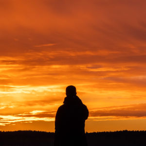 Henkilö meren jäällä katsoo auringonlaskua.