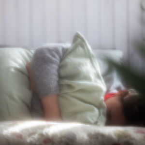 Henkilö makaa sängyn päällä käpertyneenä tyynyä puristen.
