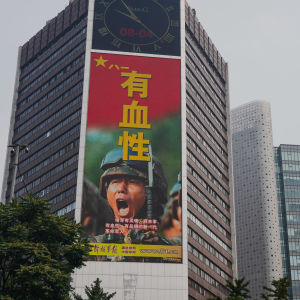 Rakennuksen seinän korkuisessa mainoksessa on sotilaan huutavat kasvot ja teksiä kiinaksi.