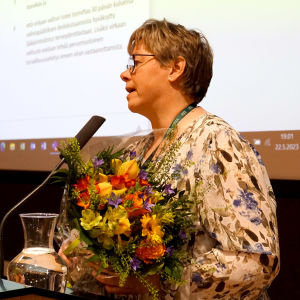 Kvinna står i en talarstol och håller i en blombukett.