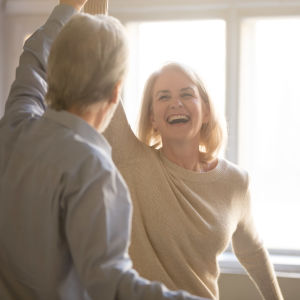 En äldre man och kvinna dansar leende hemma.