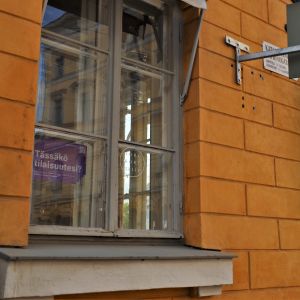 Ett litet fönster i förgrunden med en lapp som annonserar att affärslokalen uthyres. I bakgrunden syns Helsingfors domkyrka.