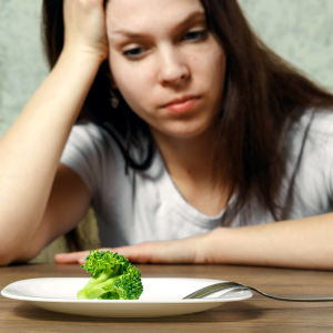 ung kvinna tittar på en tallrik med en bit broccoli