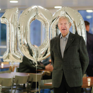 Jaakko Estolas hundraårsdag firades med pompa och ståt bland spelkamraterna. Hundraåringen Jaakko Estola poserar framför silverballonger med siffrorna 100.