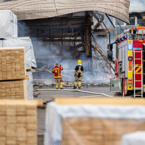 Kaksi palomiestä katsovat palossa tuhoutuneeseen varastorakennukseen Mustola Timber -sahalla Lappeenrannassa.