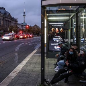 Passagerare i munskydd väntar på en busshållplats i Berlin.